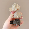 Hand holding three rhinestone high ponytail clips in gold, silver, and black, featuring a tiara-inspired design with crystal embellishments and pearl accents.