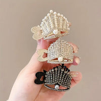 Hand holding three rhinestone high ponytail clips in gold, silver, and black, featuring a tiara-inspired design with crystal embellishments and pearl accents.